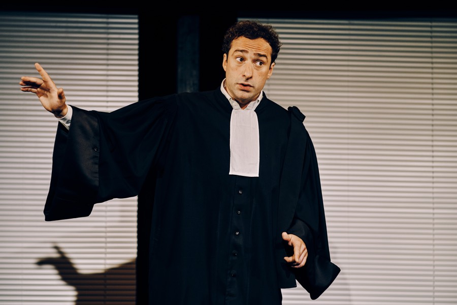 En robe d'avocat, en pleine plaidoirie devant des stores
